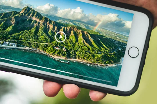 A person holding a cellphone with a beautiful Hawaiian landscape of Diamond Head displayed on the cellphone