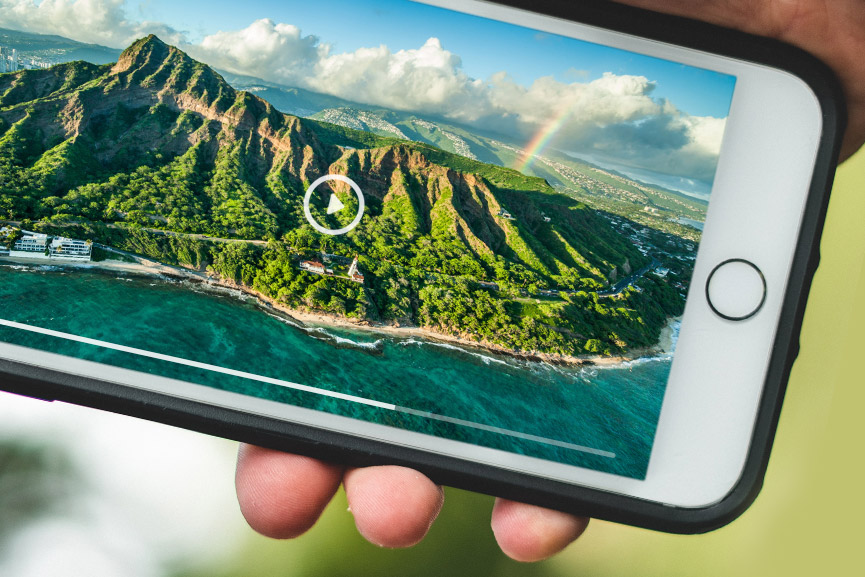 A person holding a cellphone with a beautiful Hawaiian landscape displayed on the cellphone