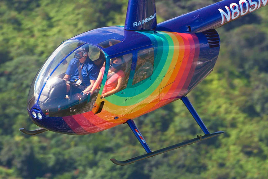 Rainbow Helicopters Oahu Robinson R44 helicopter flying above lush green forest in Hawaii