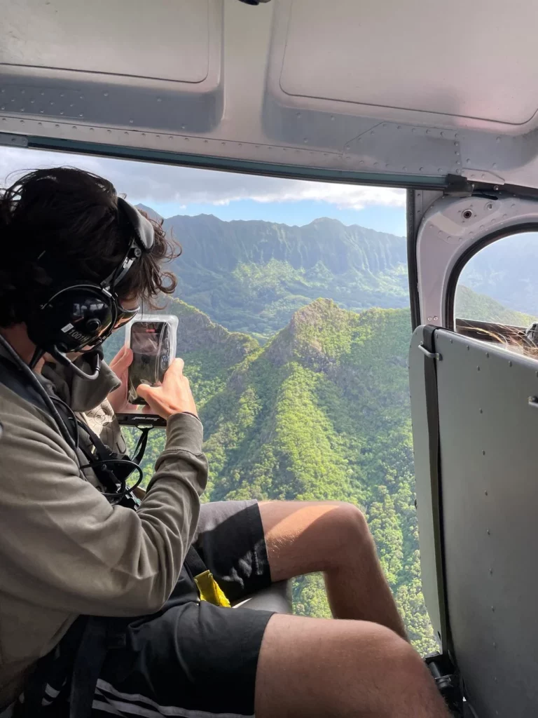 Young man taking picture of Oahu landscape from open door helicopter tour