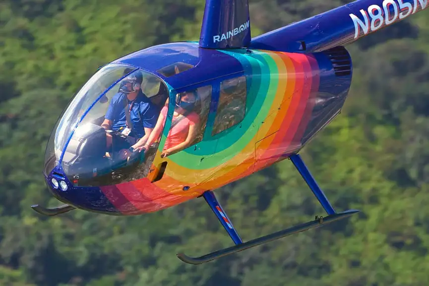 Rainbow Helicopters Oahu Robinson R44 helicopter flying above lush green forest in Hawaii