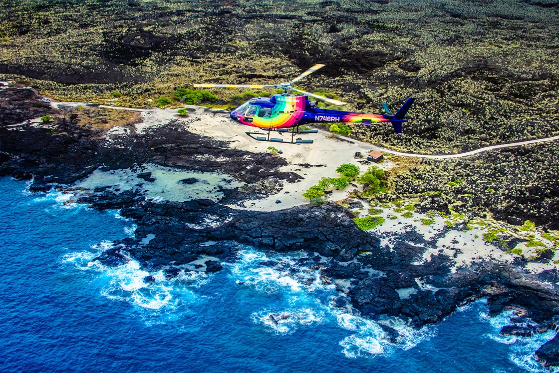 Big Island Helicopter Tours. Rainbow Helicopters Airbus Astar helicopter flying over Queens Bath Beach on the Kona coastline.